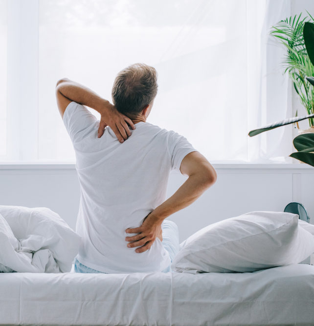 back view of man sitting on bed and suffering from back pain