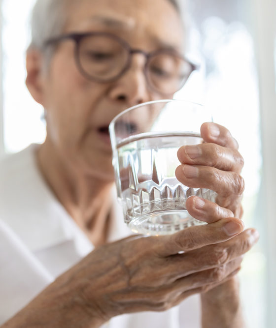 Senior woman holding glass of water,hand shaking while drinking water,elderly patient with hands tremor uncontrolled body tremors,symptom of essential tremor